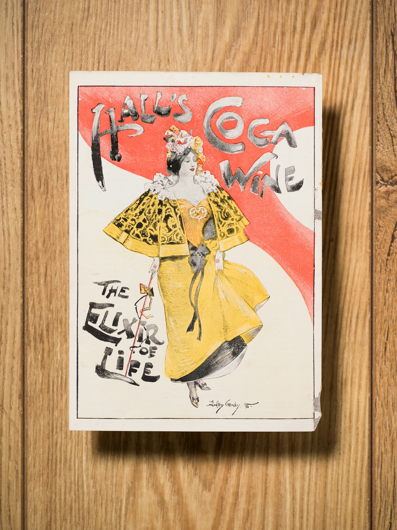 Photograph of a item of ephemera in the Wellcome library on a wooden tabletop. The advert reads, "Hall's Coca Wine, the elixir of life".