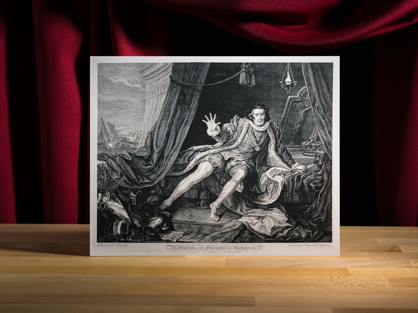 Black and white etching with engraving showing David Garrick in the role of Richard III, awakening from his nightmare in the tent with military activities in the background. His hand is raised a his fingers are splayed outwards. He has an expression of bewilderment. 