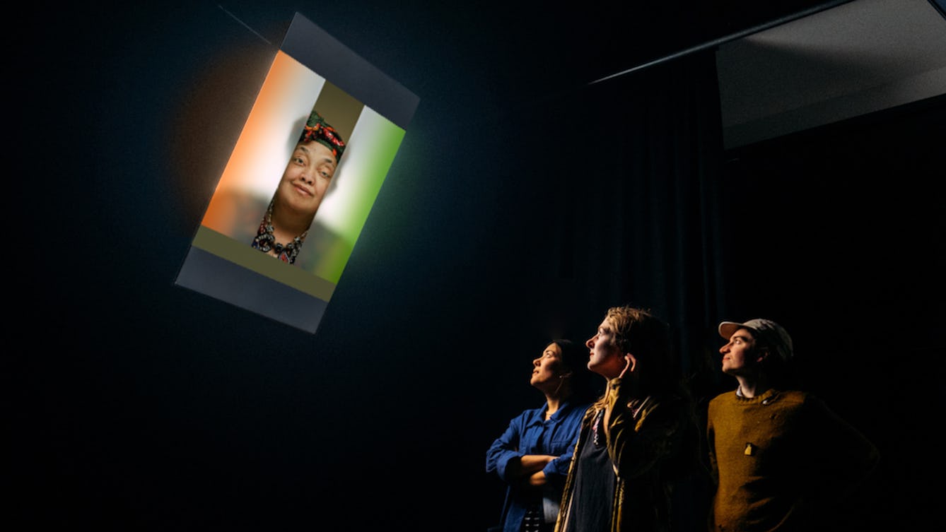 Photograph of three people in a dark room looking at a TV screen which is showing a photographic portrait of a woman.
