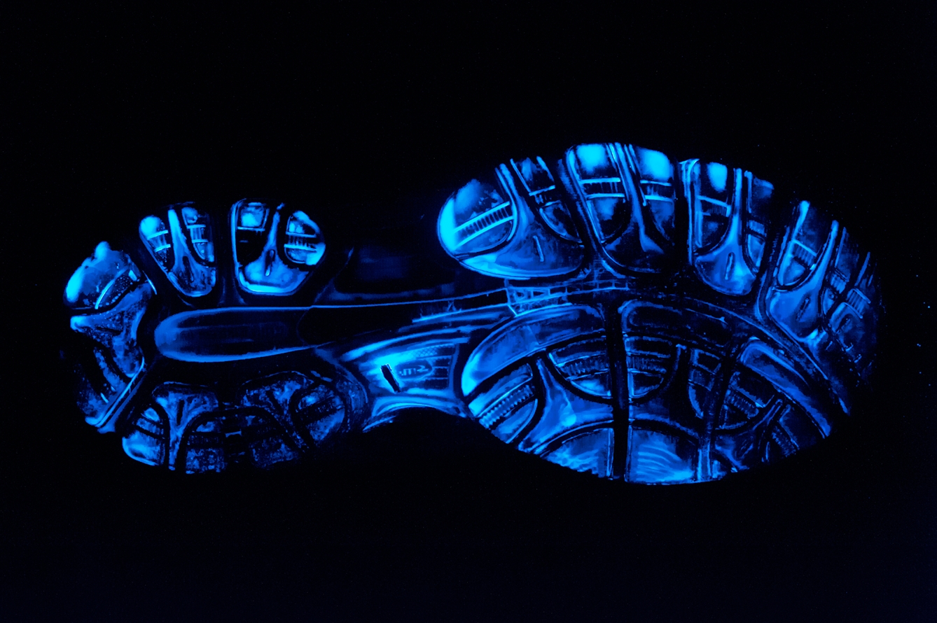 Photograph of the sole of a training shoe which has been treated with luminol to reveal extensive blood traces. These traces show up as bright blue in colour.