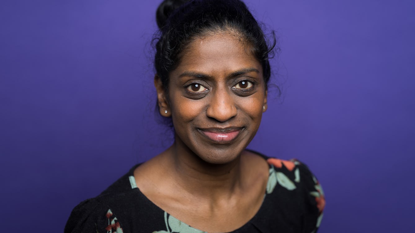 Head and shoulders photographic portrait of Nadia Nadarajah on a purple background.