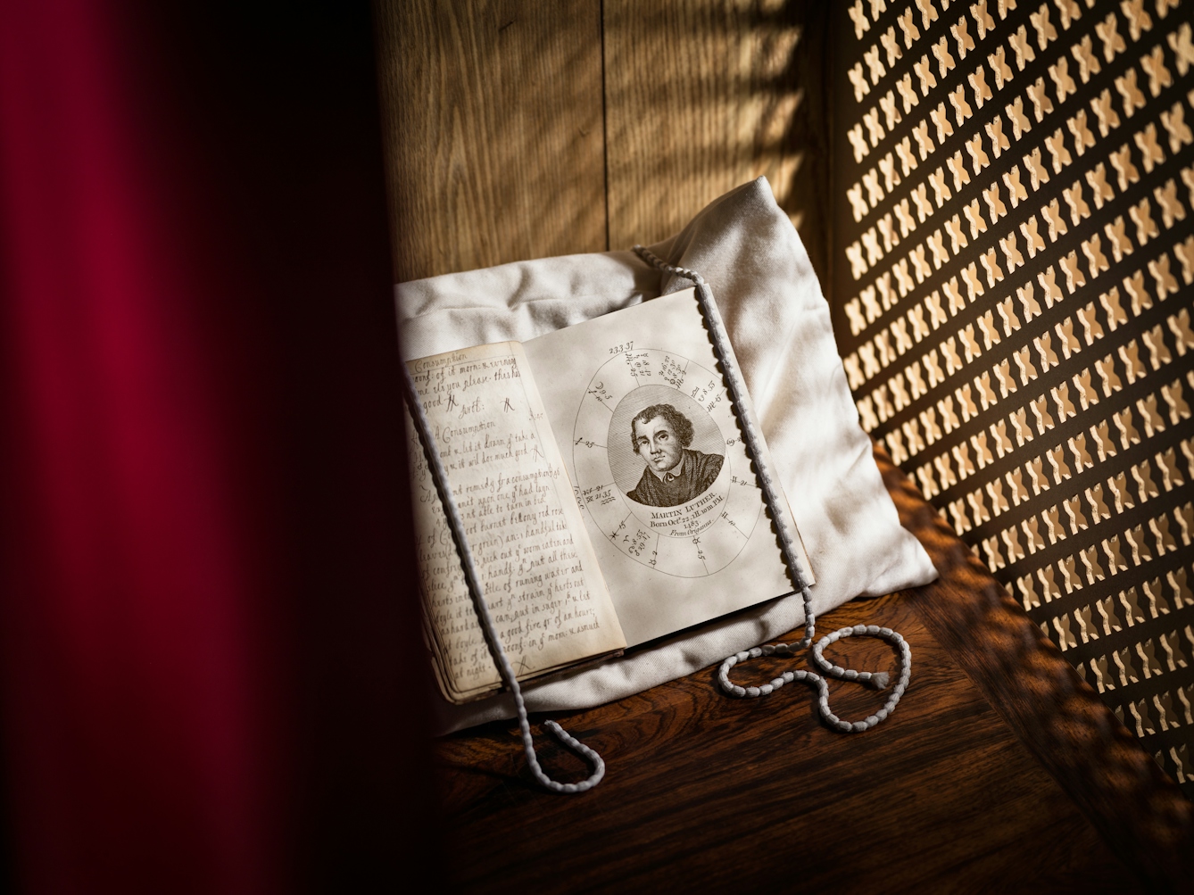 Photograph of a old book resting on a white pillow, in a confessional box. The book is open at a page showing a portrait of Martin Luther, the leader of the Protestant Reformation. To the right is the confessional screen with light streaming through. To the left is the hint of a red curtain.