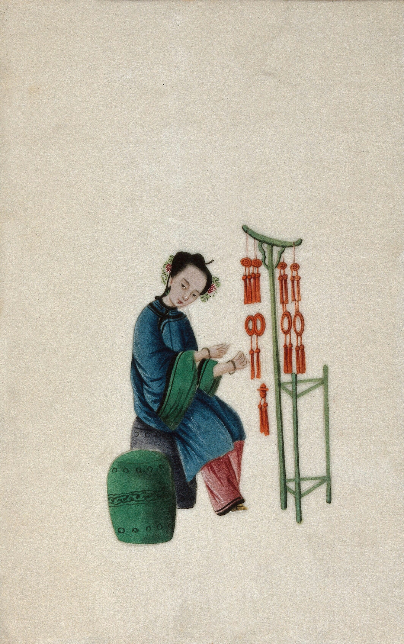 A 1800s watercolour painting of a woman displaying good luck tassels for sale. The tassels are red and are hanging on a green stand. 

The woman is sat upon a gray stool, there is a green stool next to her. She is wearing a blue dress over red trousers. 