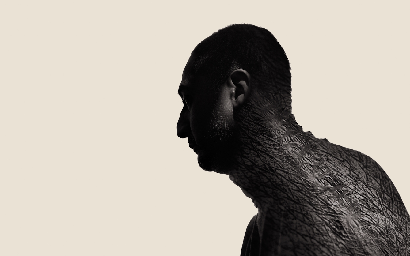Photographic portrait of a man's head and shoulders in profile, looking to the left. He is pictured in silhouette against a cream background. Overlaid onto his neck and shoulders is an image of a scar, showing the texture of the skin and the scar tissue. 