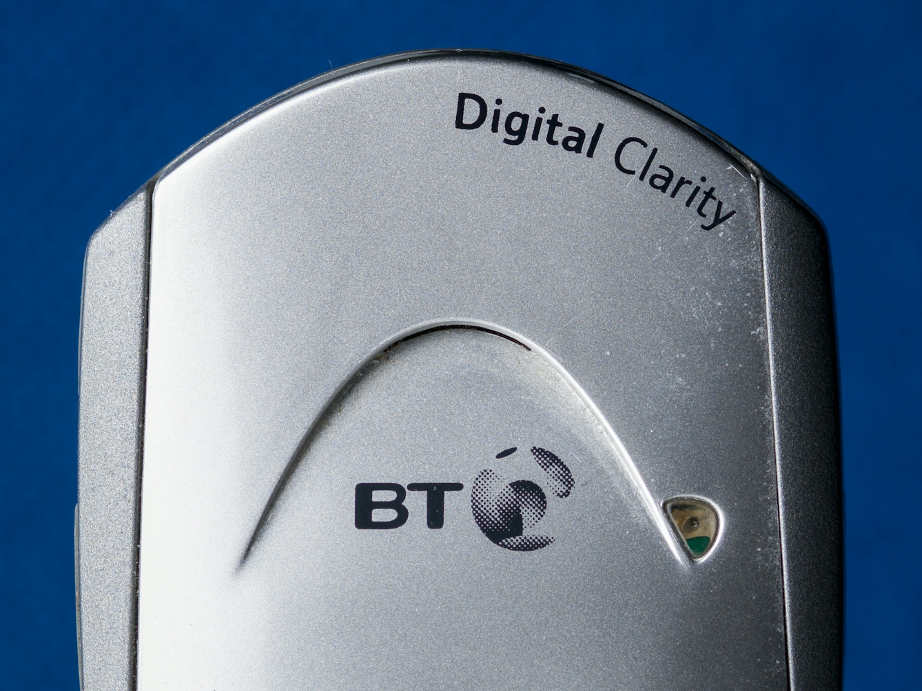 Photograph of a close up of a telephone receiver's earpiece, against a blue felt background. On the receiver's display is the text 'base 1' and printed on the top of the phone are the words, 'Digital Clarity'.