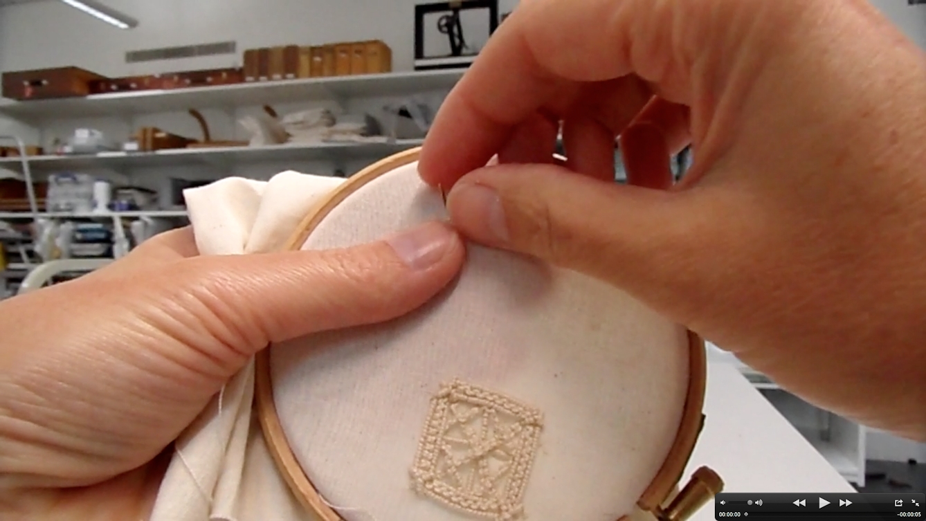 Photograph showing a pair of hands sewing with a needle onto an embroidery hoop. At the bottom of the hoop, there is an embroidered square with stitches in it in a pale cream thread. 