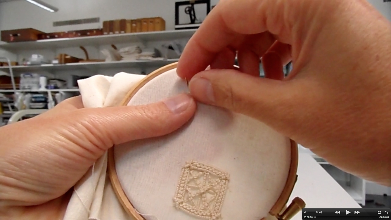 Photograph showing a pair of hands sewing with a needle onto an embroidery hoop. At the bottom of the hoop, there is an embroidered square with stitches in it in a pale cream thread.
