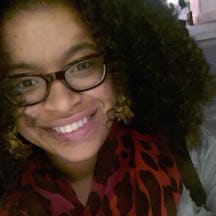 Photograph of a young woman, leaning into the camera, wearing glasses and a red and black scarf.