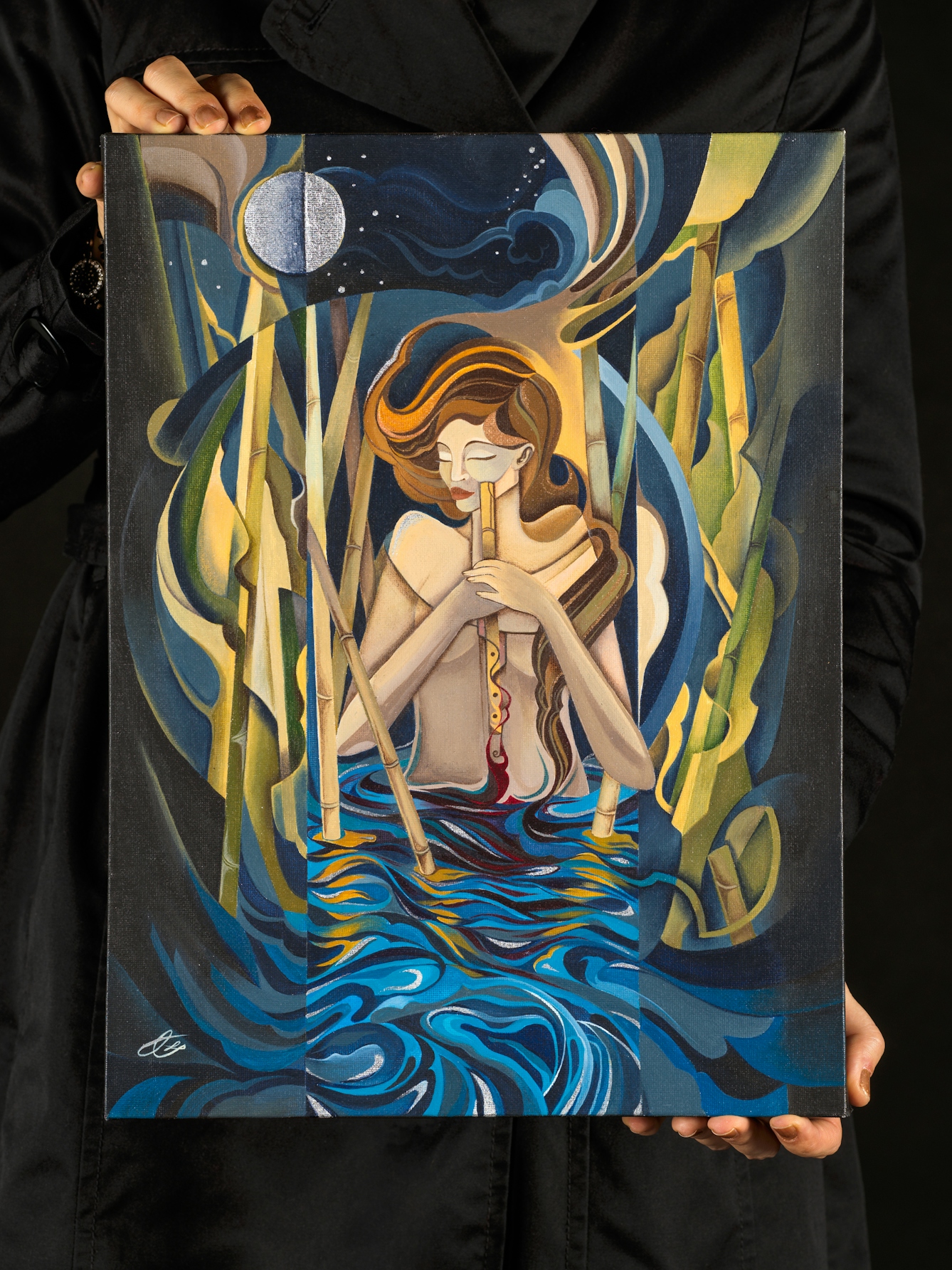 Photograph of a woman in a black dress holding a rectangular artwork. The woman's head can't be seen, just her torso and hands. The artwork is acrylic paint on canvas and shows a stylistic portrayal of a woman stood waist high in water. She is surrounded in the water by reeds and a bright moon shines down from the night sky above her. She seems to be holding a cut stem from one of the reeds, which she is holding in front of her in both hands. Her eyes are closed.