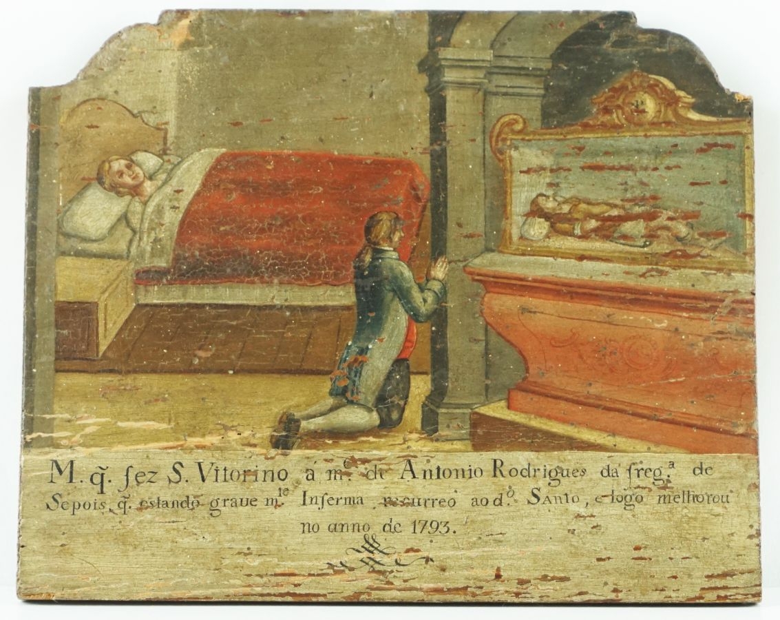 Colour photograph of a colour-painted panel showing a person kneeling at the bedside of a smiling person, beside which is a painting of St Victorinus, who lays in a position similar to the person in the bed. 