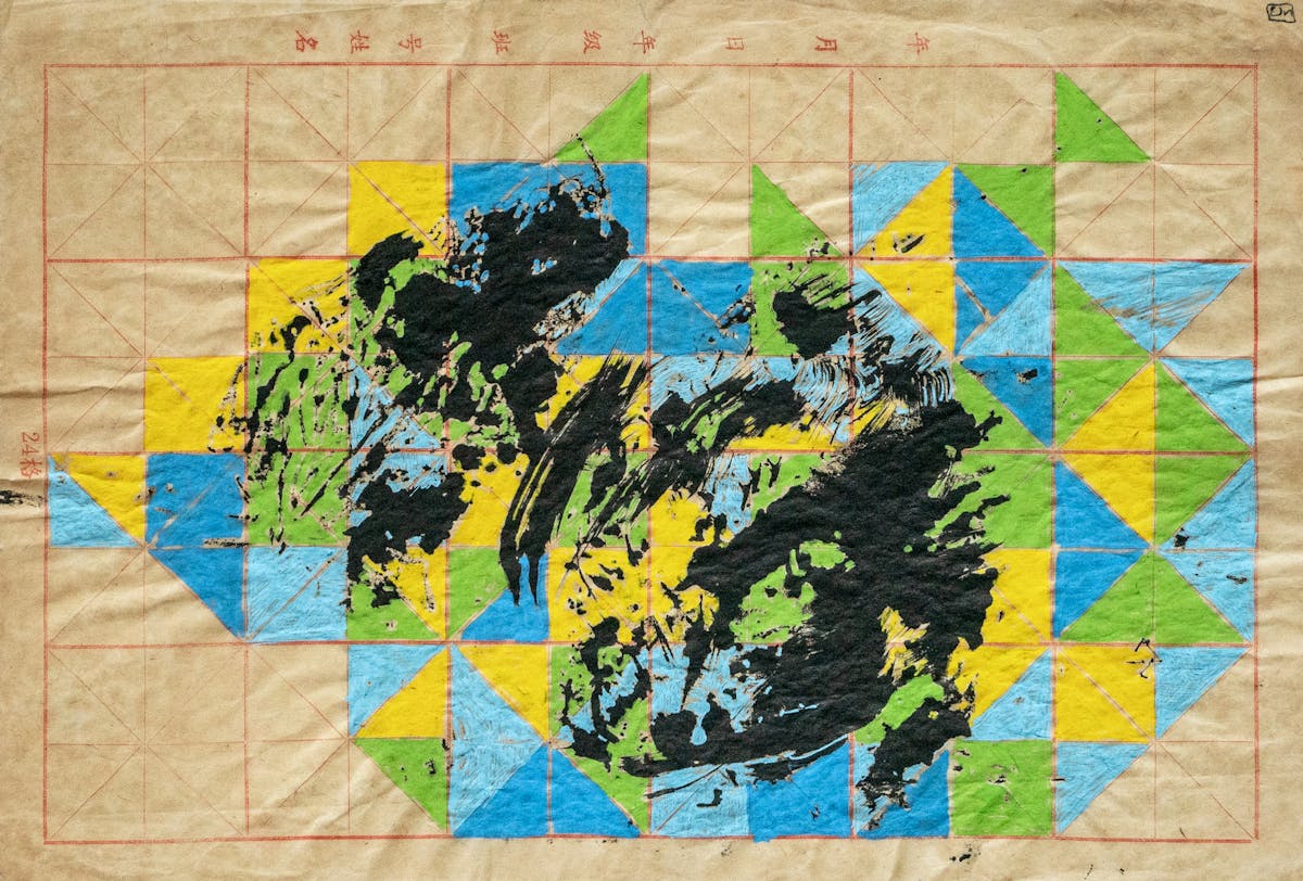 Photograph of an abstract drawing on pink gridded Chinese calligraphy paper that is slightly crumpled and folded. Many of the triangles within the grid are filled in with turquoise, light blue, light green and yellow ink. There is a an abstract mass of black ink in the middle, which shows the traces of the artist's brushstrokes. Above the grid are some small pink Chinese characters. 