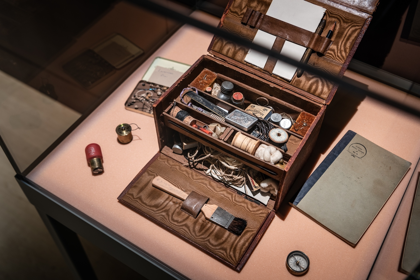 Photograph of an open wooden box containing lots of small items, in a display case as part of the Smoke and Mirrors exhibition at Wellcome Collection.