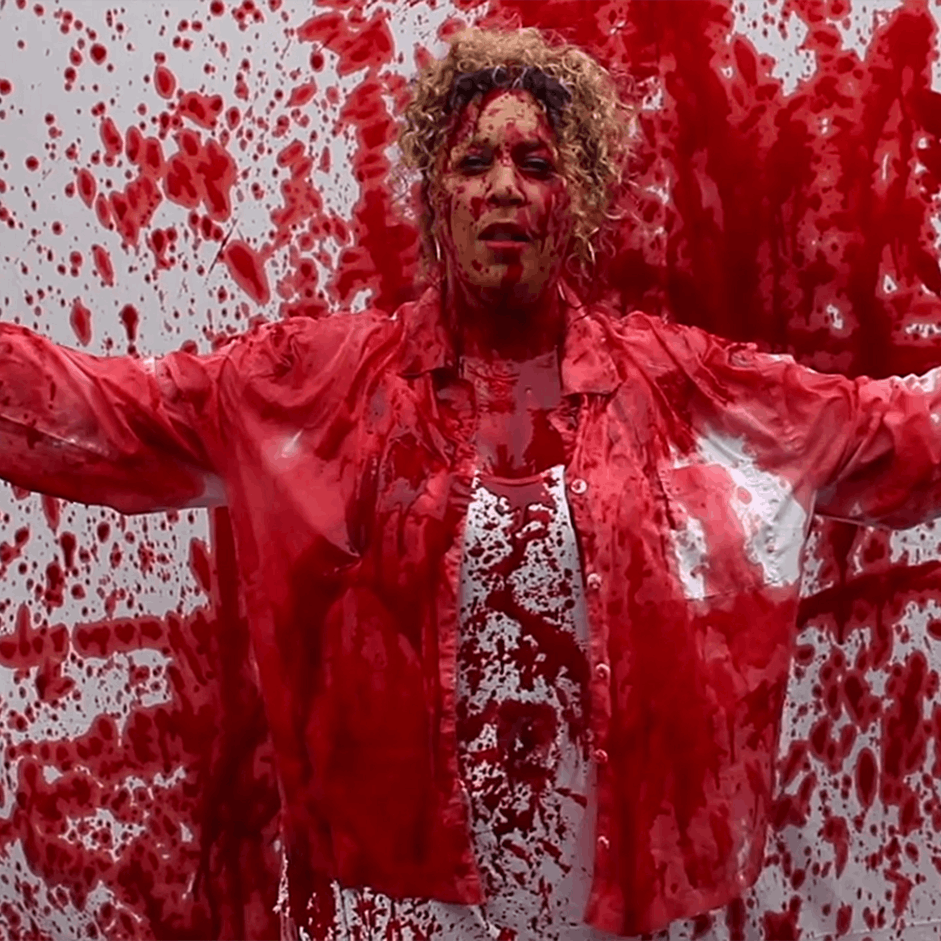 Salena Godden standing against a backdrop splattered with red paint