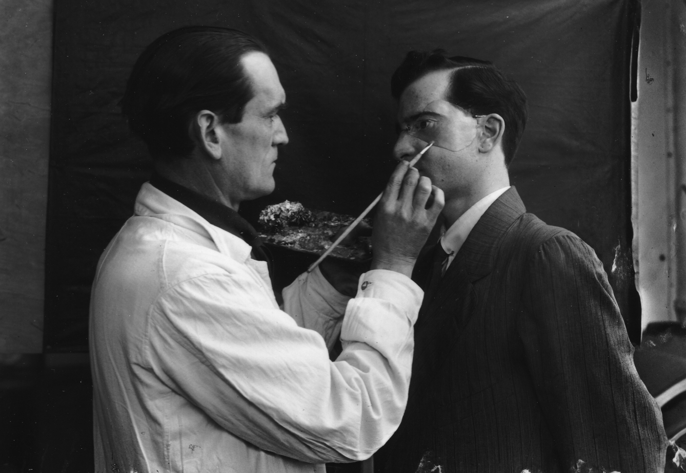 Captain Francis Derwent Wood holds an artist's palette as he adds the finishing touches to a patient's new facial plate.