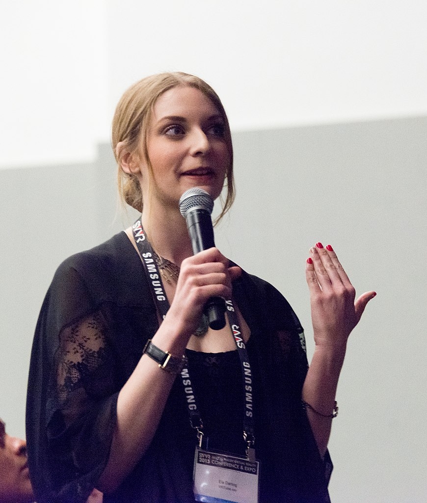 Colour photograph of Ela Darling holding a microphone and asking a question whilst wearing a conference lanyard.