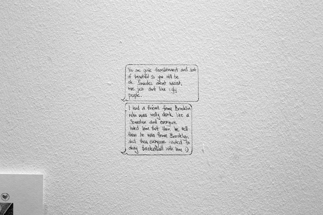 Photograph of an artwork in a gallery. The artwork is a pencil drawing of two speech bubbles, recreating comments the artist has received on Tinder.