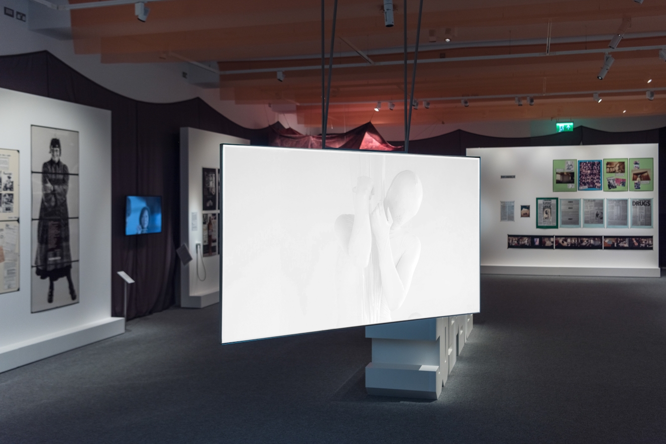 Photograph of the Misbehaving Bodies exhibition at Wellcome Collection, showing a wide view of the space. In the foreground is a video piece by Oreet Ashrey titled 'Revisiting Genesis' which is projected onto a large screen.
