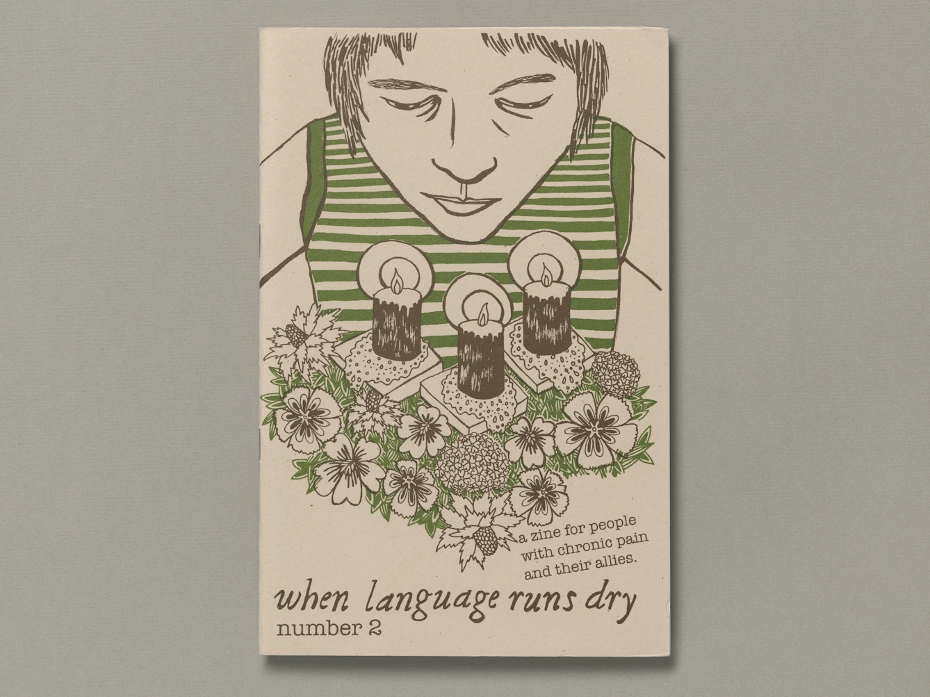 A young person leans forward over an arrangement of three lighted candles on a bed of flowers and foliage. The text below the illustration reads "when language runs dry, number 2"