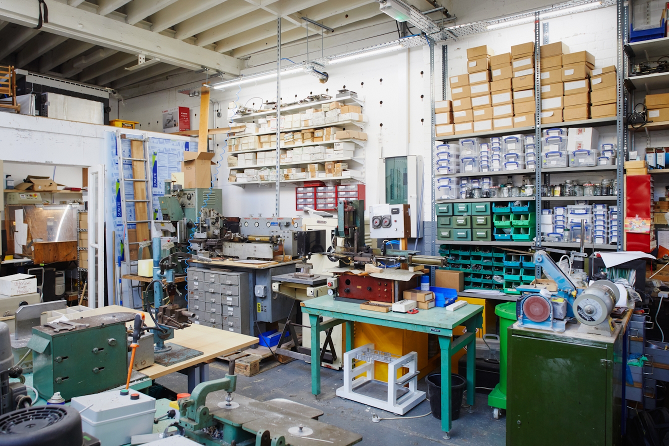 Photograph of a workshop space filled with tools, workbenches, equipment and boxes of parts, all neatly arranged on shelves and in cupboards.