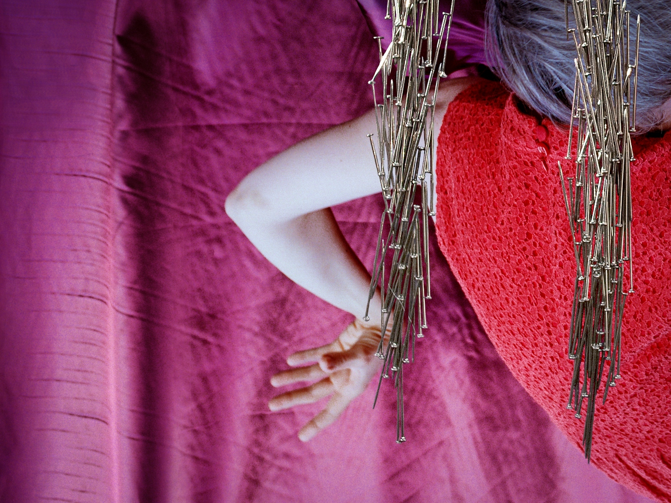Detail from a larger artwork created with a colour photographic print of a female figure in a bright red dress, set against a purple and blue draped silk background. The detail shows the woman's bent arm and two of the pillars made out of dress pins.