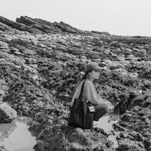 Black and white photograph of Angela Chan knelt down on rocky terrain. 