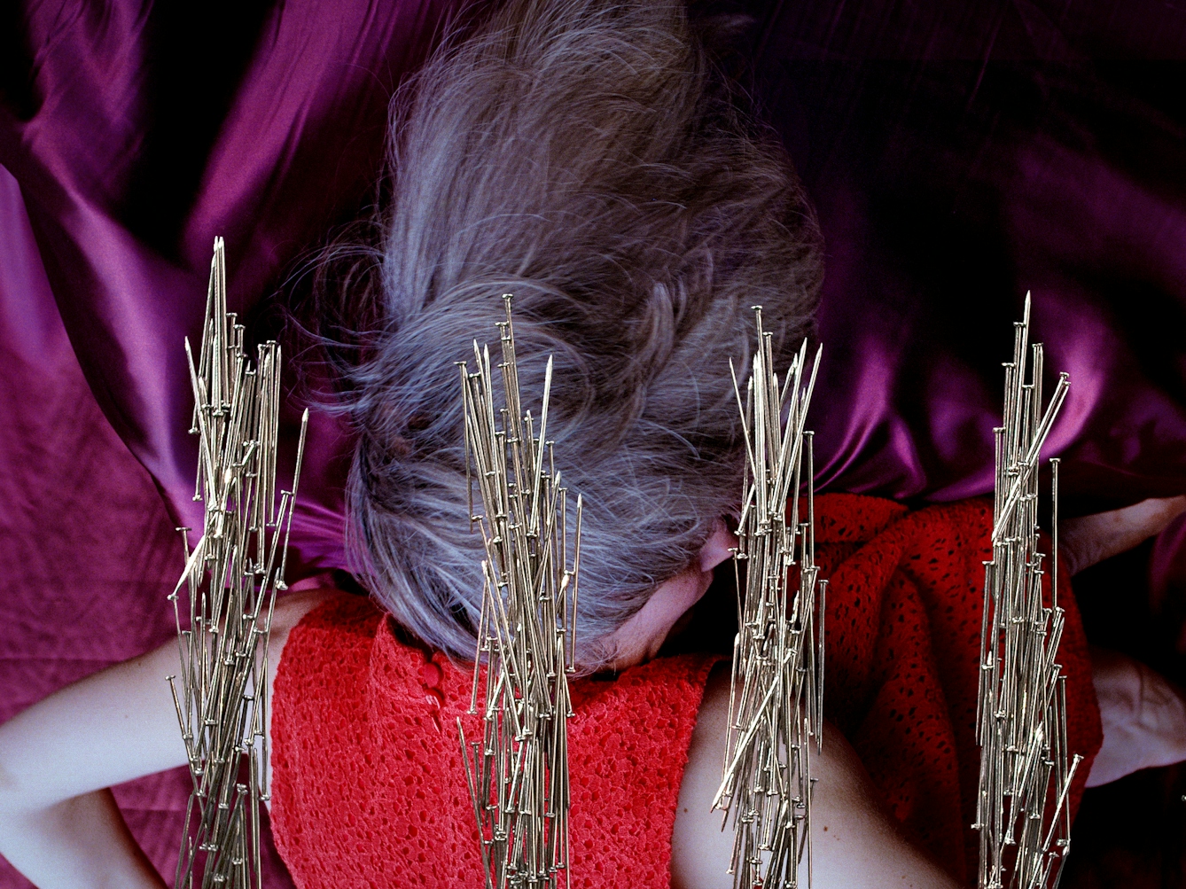 Detail from a larger artwork created with a colour photographic print of a female figure in a bright red dress, set against a purple and blue draped silk background. The detail shows the woman's head and part of the 4 pillars made of dress pins.
