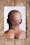 Photograph of a photographic print on a weathered, paint spattered wooden floor. The print shows the naked back of a man's head and neck against a white background. Superimposed on his back is a simple line map in white, yellow and orange, outlining different regions.