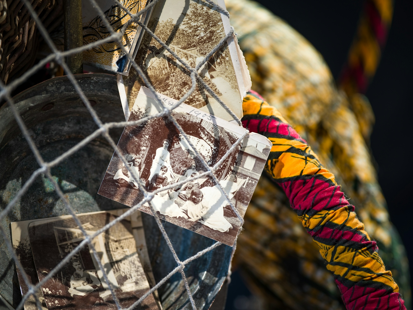 Photograph of a close-up detail of the net being carried by a life-size artwork of a figure resembling an astronaut. Within the net is a collection of black and white photographic prints showing family scenes from the early 20th century.