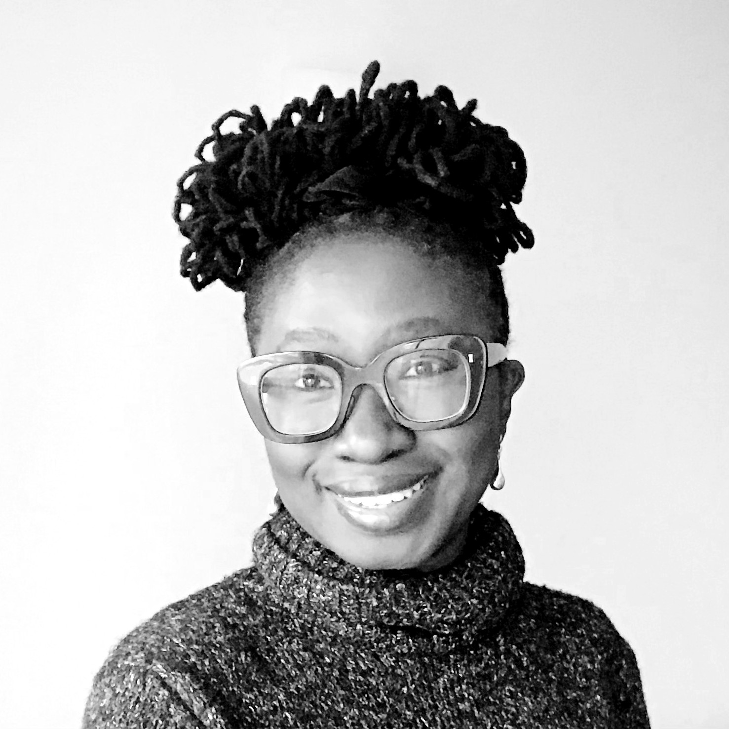Black and white photograph of a young woman with large-rimmed glasses. She is smiling and looking directly at the camera.