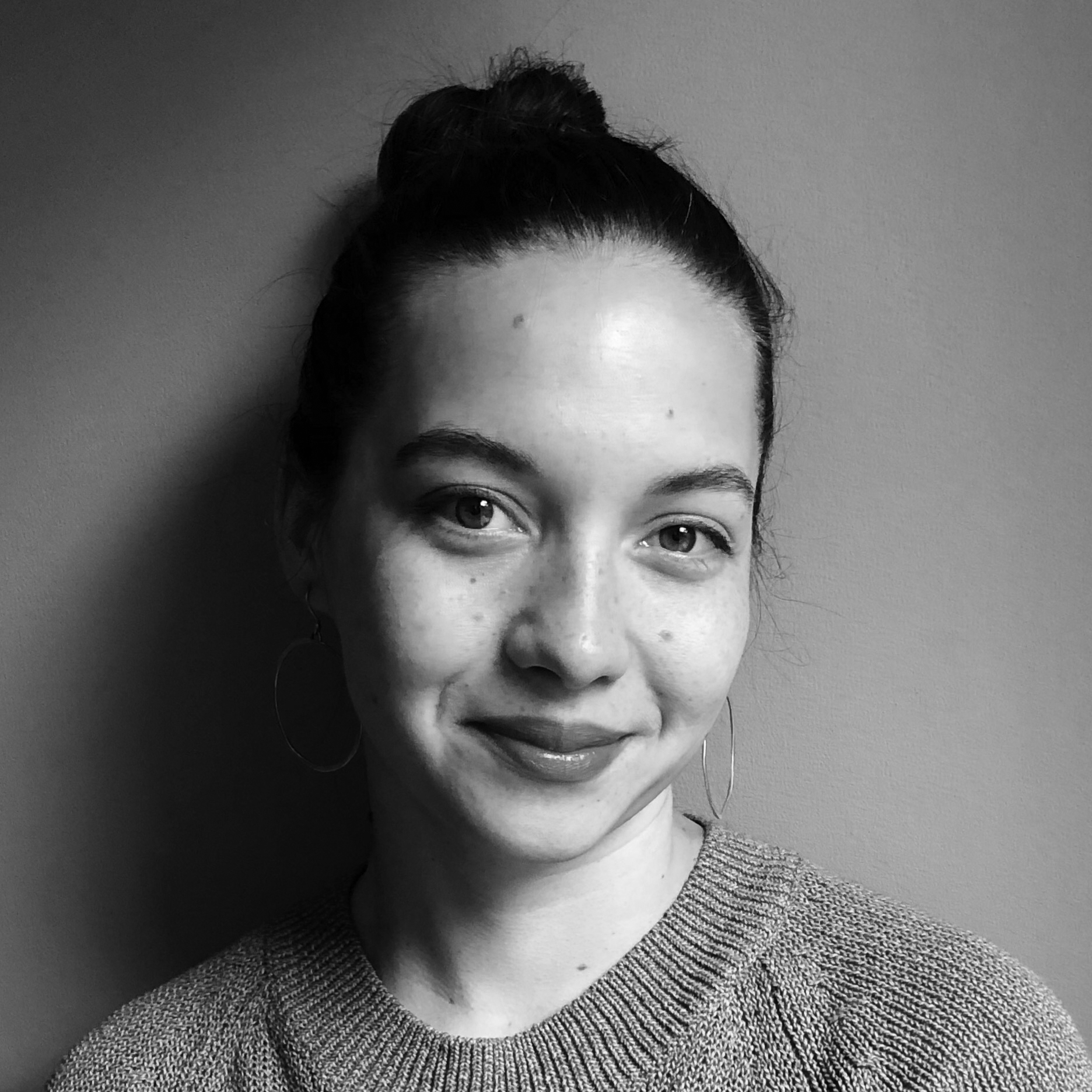 Head and shoulders photograph of a young woman, smiling, with her hair in a bun and large hoop earrings.