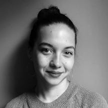 Head and shoulders photograph of a young woman, smiling, with her hair in a bun and large hoop earrings.