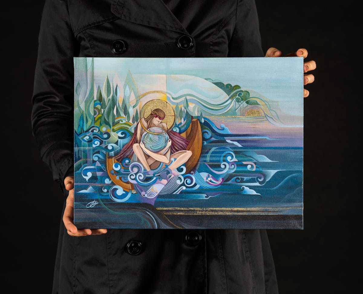 Photograph of a woman in a black dress holding a rectangular artwork. The woman's head can't be seen, just her torso and hands. The artwork is acrylic paint on canvas and shows a stylistic portrayal of a woman sat cross legged in a wooden boat surrounded by swirling water. She is clutching a globe-like shape in her arms and her head is bowed. She seems to have golden halo around her head. Behind her in the distance are the green shapes of land and trees, and a sun setting over the watery horizon.