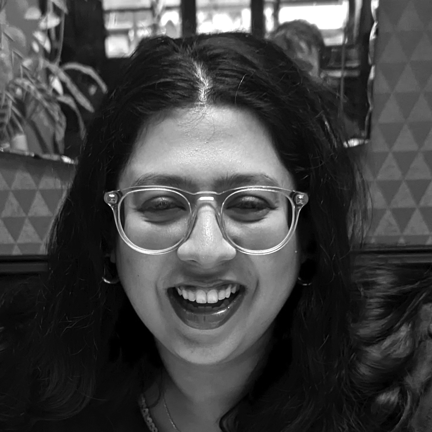 Head and shoulders photograph of a young woman with wavy long dark hair wearing glasses and smiling.