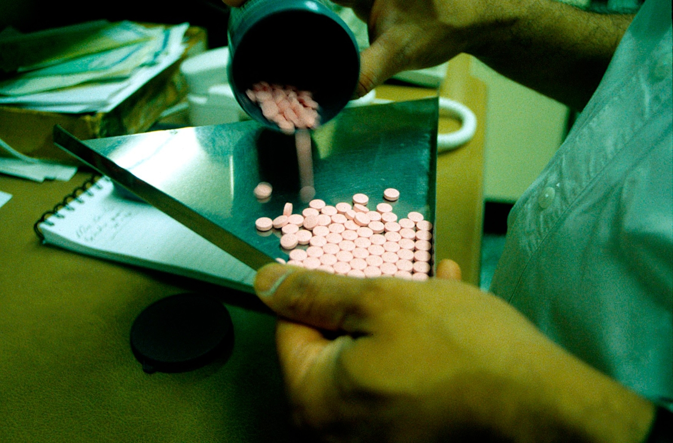 Shows chemist's hands tipping pink tablets into metal triangular tray prior to counting into bottles.