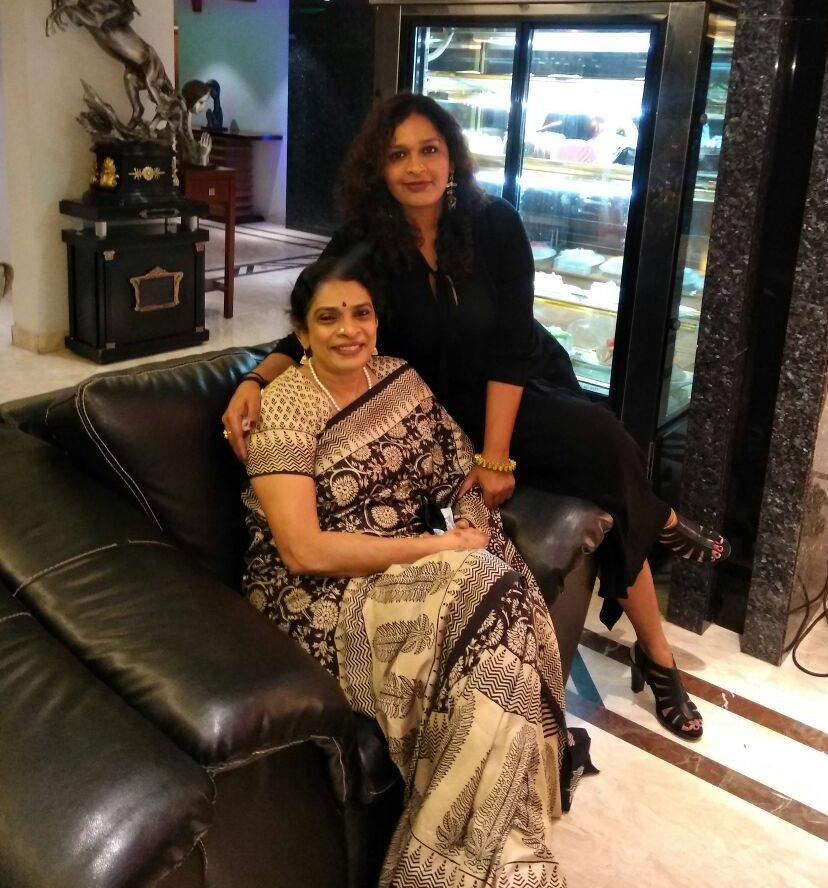 Two Indian women sat on a sofa posing for a photograph in their living room