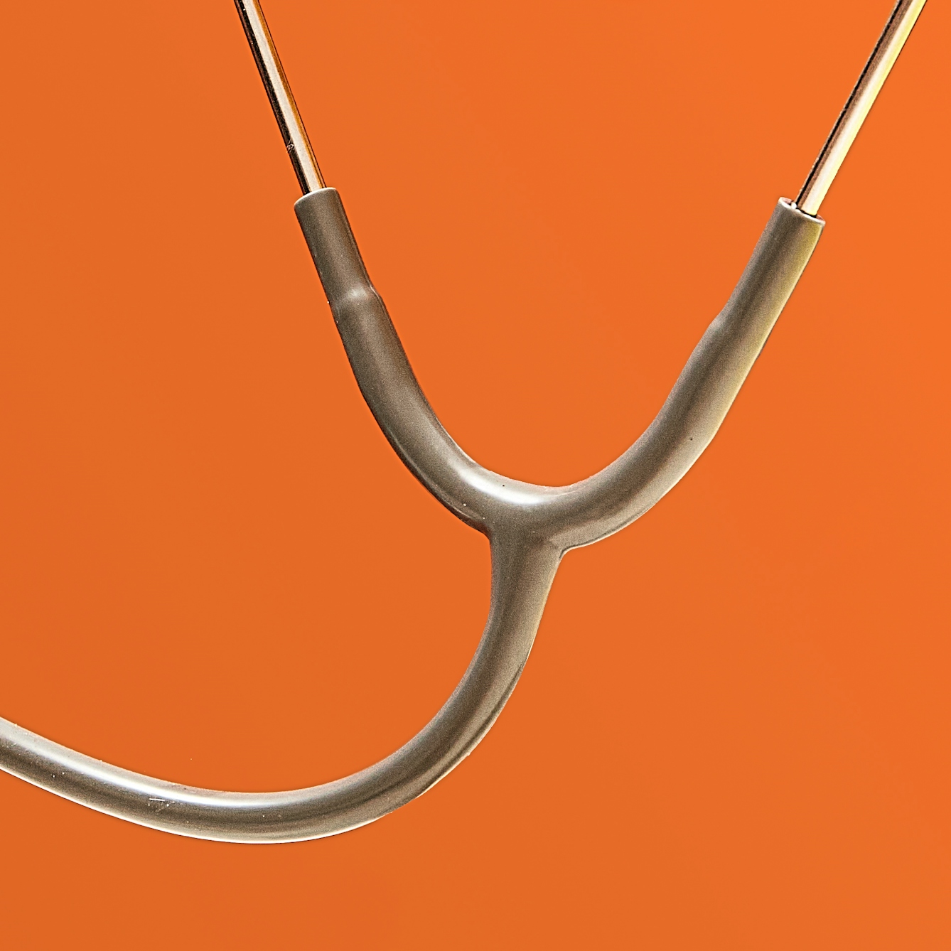 Photograph of a section of a grey stethoscope floating in front of a bright orange background.