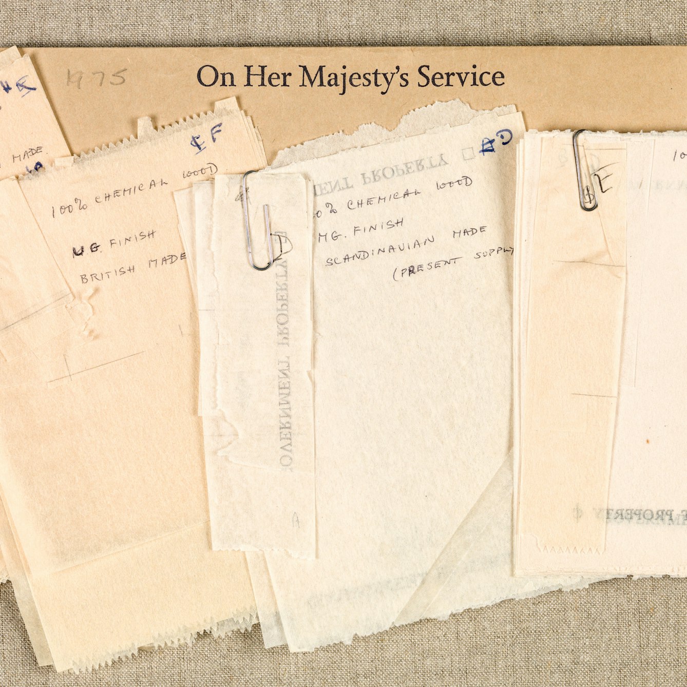 Photograph of a selection of toilet paper samples held together with paperclips, resting on a manilla envelope printed with the words "On Her Majesty's Service".