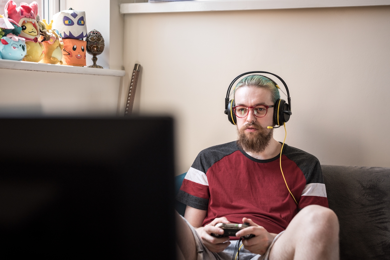 Photograph of a man wearing headphones and a microphone playing a computer game.