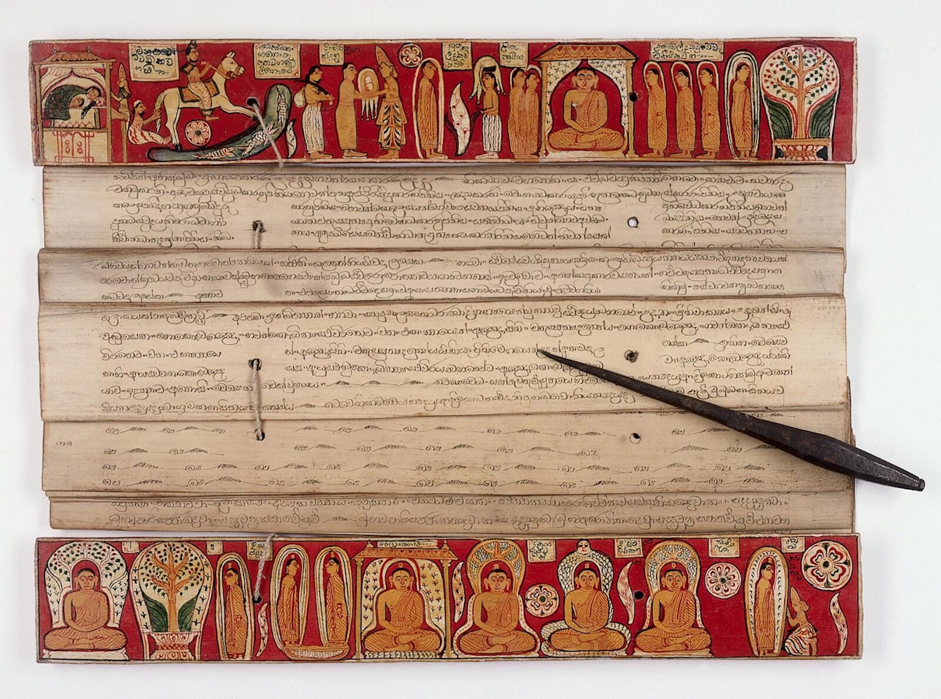 A Singhalese palm leaf manuscript with a brightly coloured painted wooden binding with images of teh Buddha. The manuscript is open to reveal the inscribed text on the palm leaves. A black wooden stylus lays across the leaves.