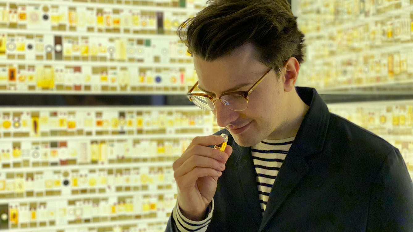 A photo of William Tullett holding a small bottle of liquid and smelling yellow translucent liquid.