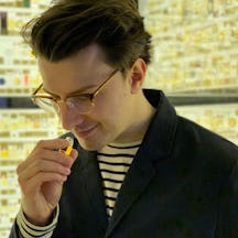 A photo of William Tullett holding a small bottle of liquid and smelling yellow translucent liquid.