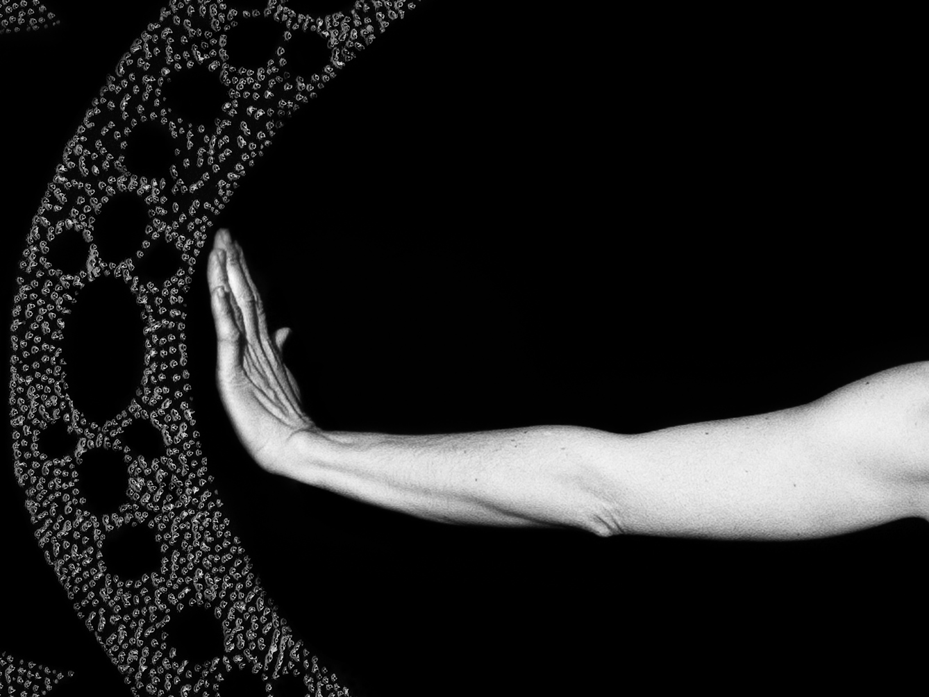 Artwork made up of a black and white photograph of a female figure from behind, from against a black background. Her left arm is held out straight to the side, her wrist and hand are held up indicating a stop action. To the left of her hand is part of a large ellipse made up of a layered texture of dots which forms a protective barrier against sharp tooth like forms approaching the barrier, also made up of layered textured dots.