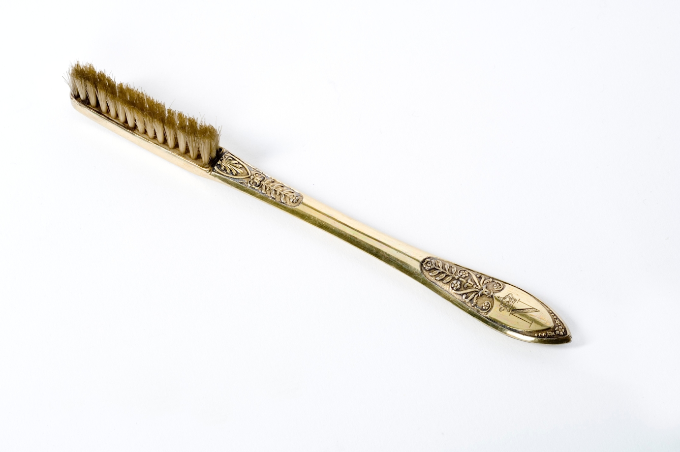 A photograph of a luxury gold toothbrush the letter ‘N’ engraved on the handle.