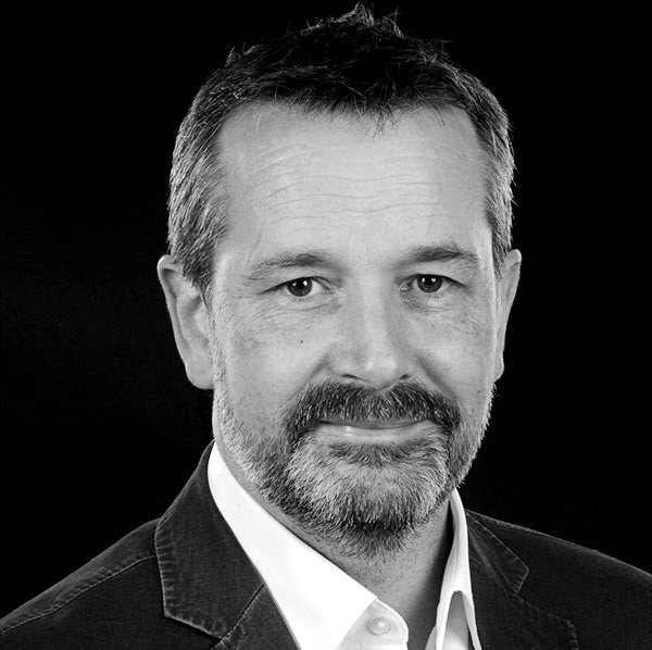 Black and white head and shoulders photograph of a middle-aged man with a short beard. The man is smiling and looking straight at the camera.