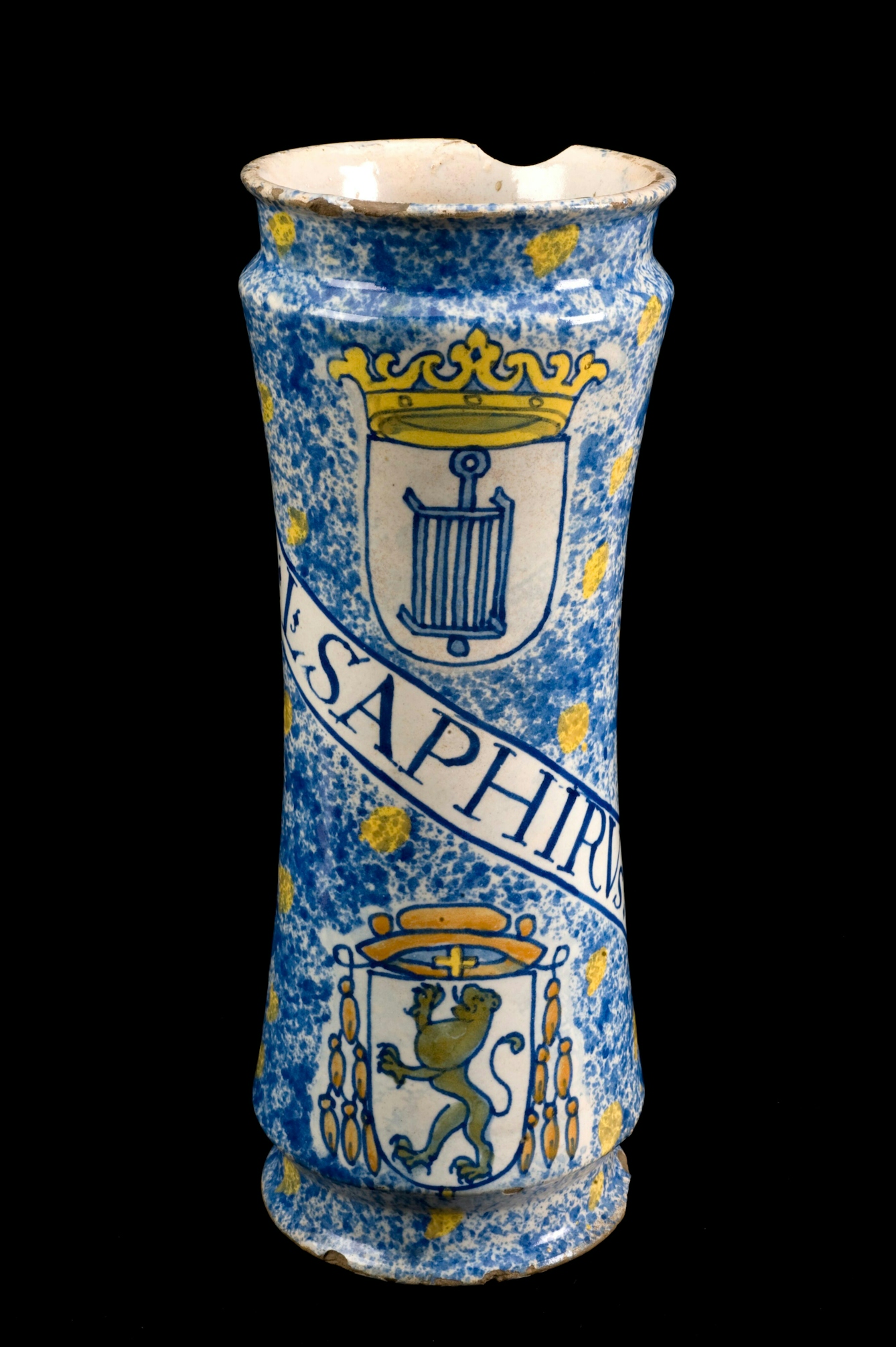 Photograph of a ceramic jar against a black background. The jar is hand painted with blue and yellow patterned elements  and symbols of a crown and a lion in a crest. Across the jar are the letters, "L SAPHIRV..."