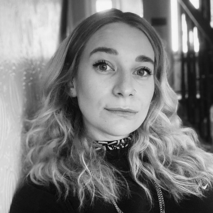 Head and shoulders photograph of a woman with shoulder-length hair, wearing a dark jumper with a necklace over the top. 