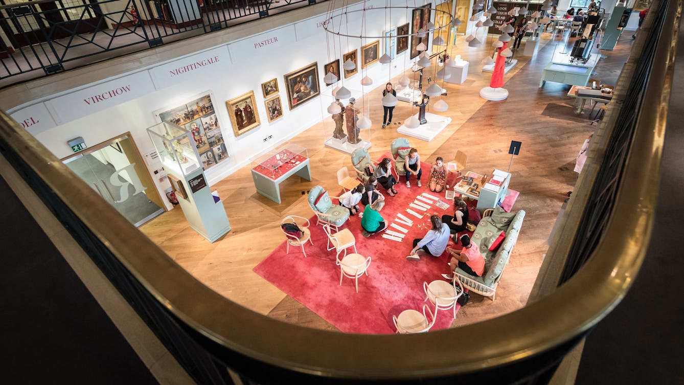Photograph of a group of people sitting in a circle on the carpet in the Wellcome Collection Reading Room, engaged in discussion.