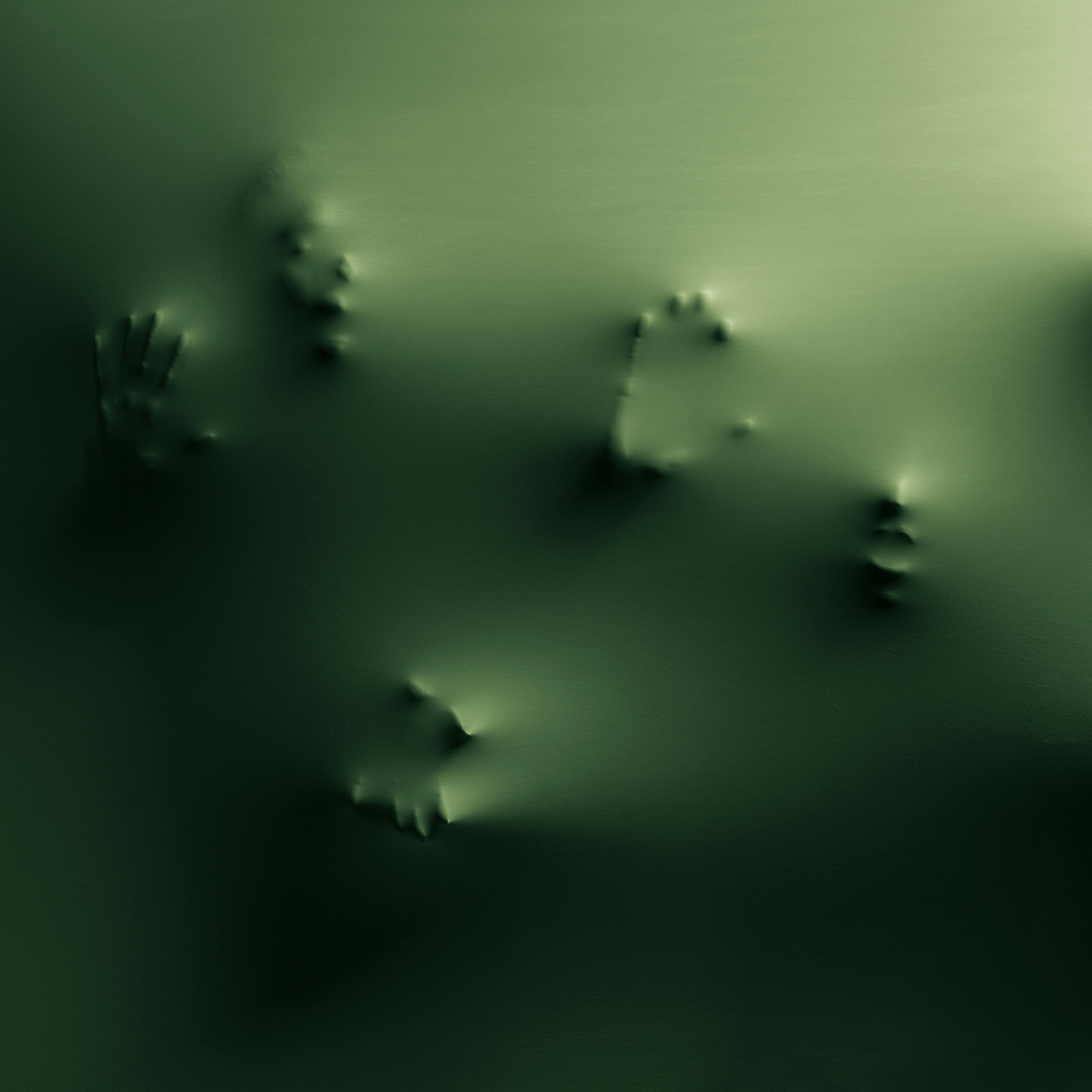 Photograph of a green membrane with three faces and five hands partially appearing in relief through it.