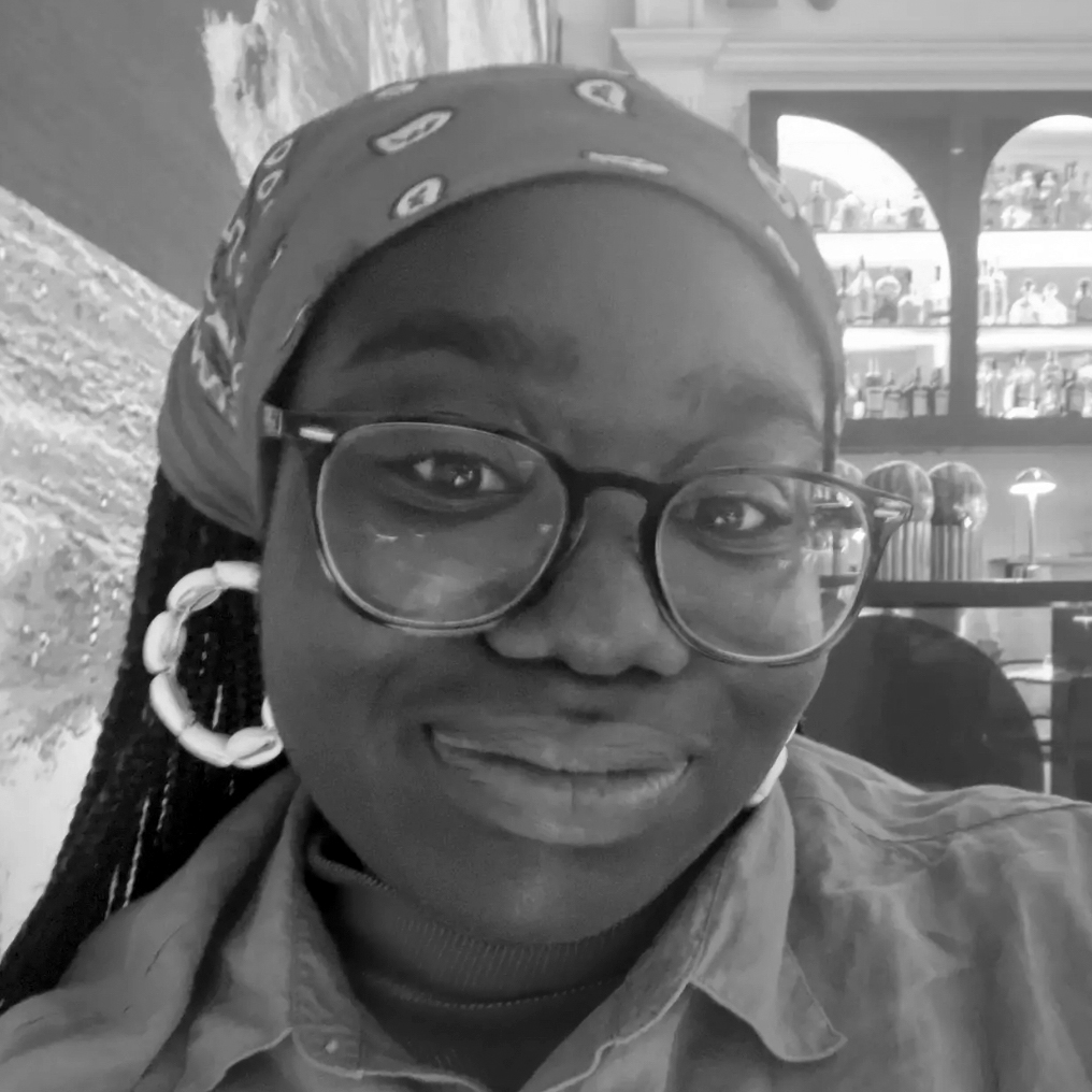 Head and shoulders photograph of a young woman, wearing glasses, with a headscarf covering long braids.