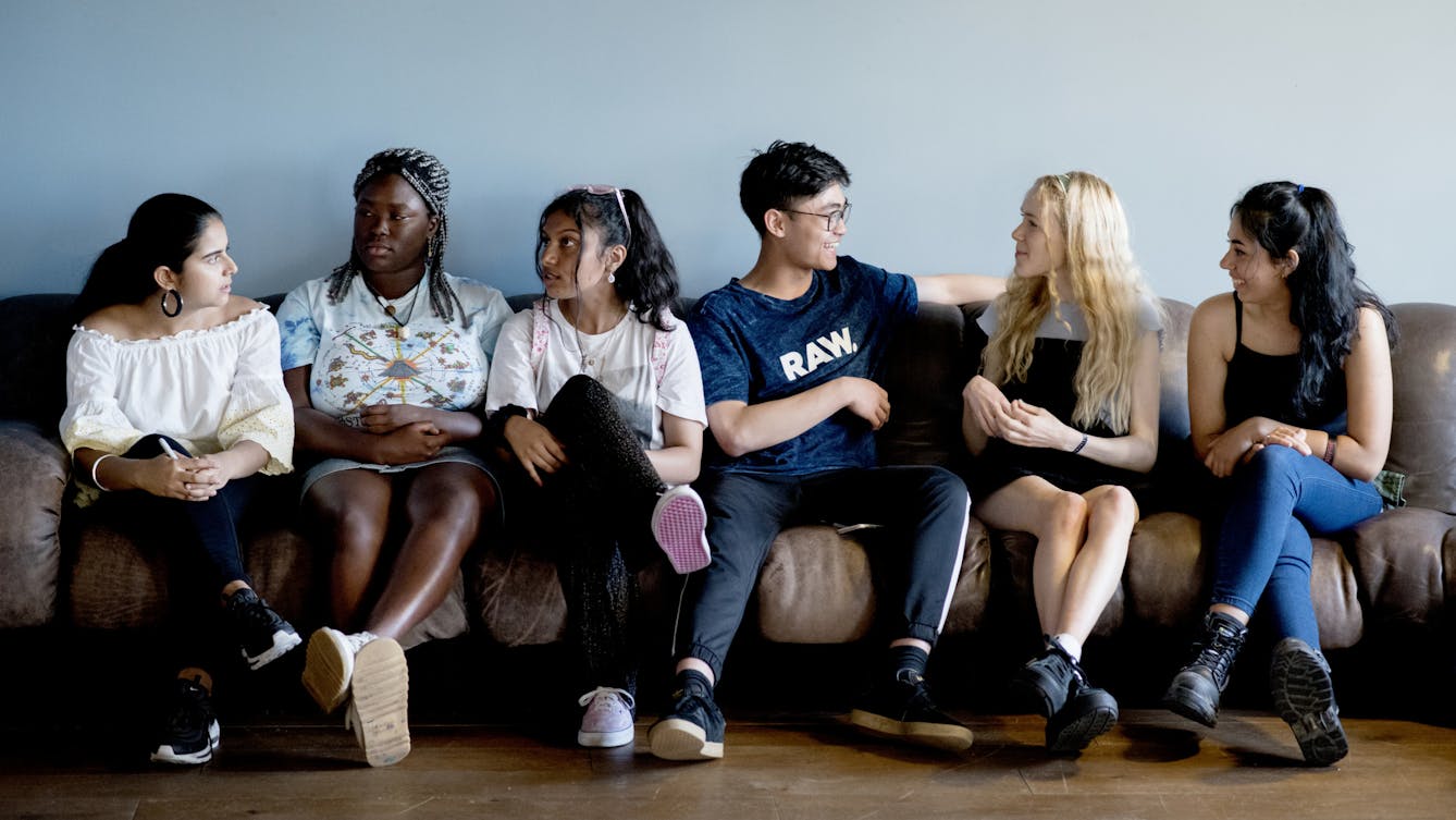 Six young people from the RawMinds Ambassadors sit on a sofa, talking to each other. 